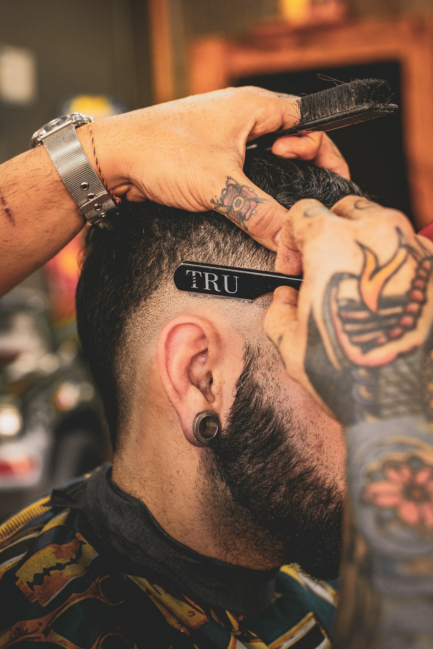 Tattooed barber's hands lining up a straight razor and trimming tools